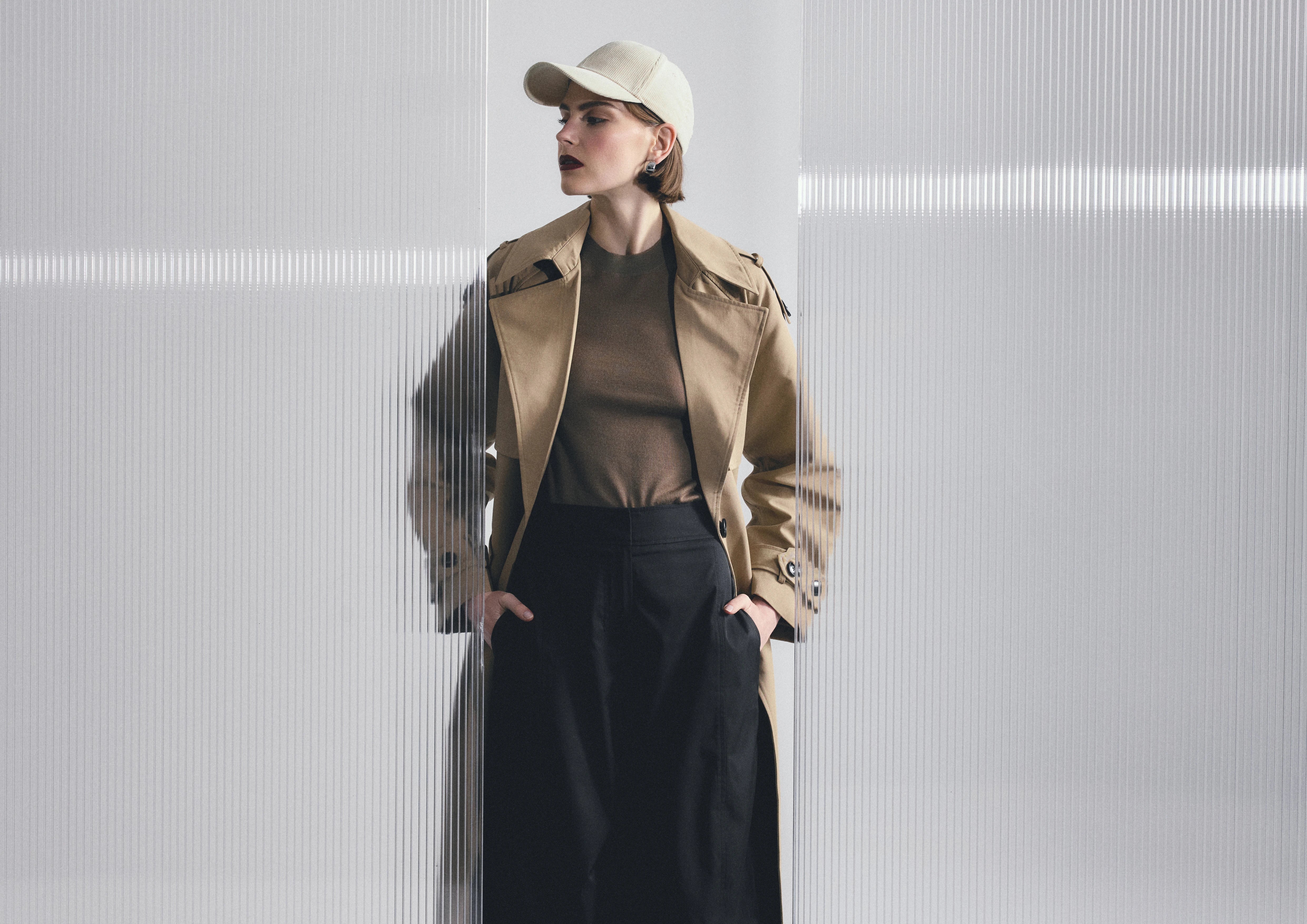 Woman wearing a beige trench coat and cap against a light gray background